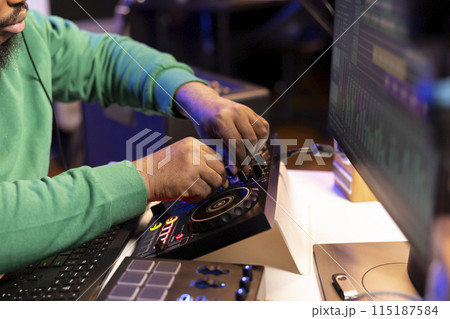 Audio engineer producing new music on mixing console in home studio, working with sound effects and pre amp knobs. Skilled producer creating songs and adjusting volume levels. Close up. 115187584