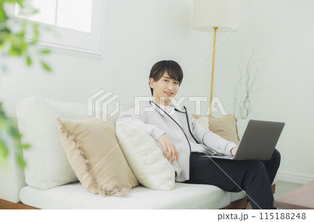 リビングでパソコンを見る若い男性 115188248