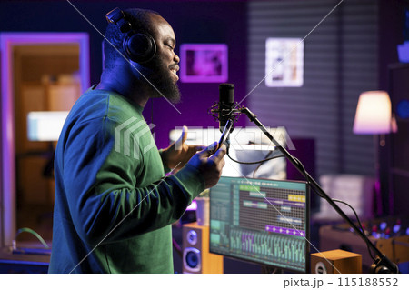 Young performer singer does a recording session for his acoustic song, performing the acapella version on microphone in home studio. Confident songwriter working on new soundtracks for an album. 115188552