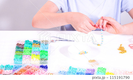 Delicate fingers of a young girl navigate through a treasure trove of bright, multicolored beads, each compartment revealing a new hue to choose from. 115191790