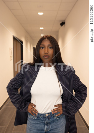 Confident woman in a white shirt, blazer, and jeans confidently poses in a hallway 115192066