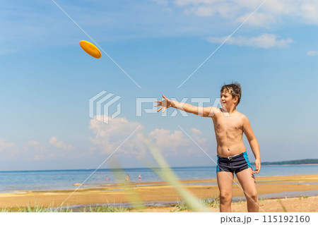 A young boy throws a frisbee on a sandy beach during a summer vacation. play, flying saucer 115192160
