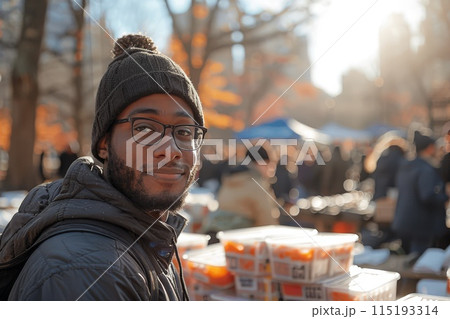 Cheerful male volunteer in glasses giving food to homeless on a street in sunny autumn day. Helping hand, support and assistance for poverty people concept 115193314