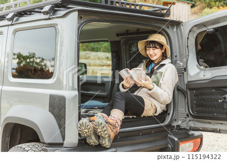 アウトドア・ハイキング・ドライブで車のラゲッジルームで本を読むアウトドアファッションの女性 115194322
