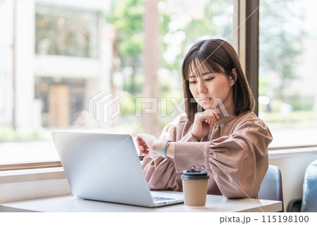 カフェでパソコンを使いながら腕時計を確認する日本人ビジネスウーマン 115198100