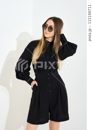 Cheerful elegant young woman in a pretty black blouse and skort touching her smooth long hair 115198711