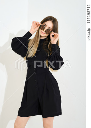 Playful young woman in black blouse and shorts playing with sunglasses 115198712