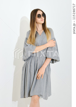 Dreamy young woman in wide grey sundress and sunglasses posing over bright background Dreamy young woman in wide grey sundress and sunglasses posing over bright background 115198717