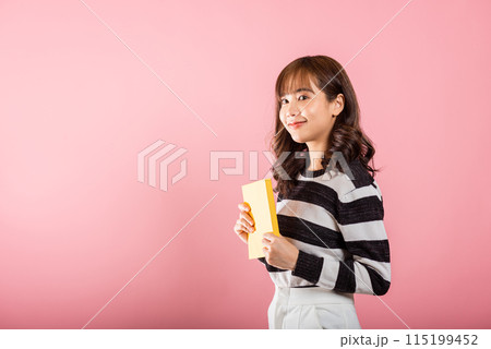 Portrait of beautiful Asian young woman teenage smiling holding a yellow book and reading, studio shot isolated on pink background with copy space Portrait of beautiful Asian young woman teenage smiling holding a yellow book and reading, studio shot isolated on pink background with copy space 115199452