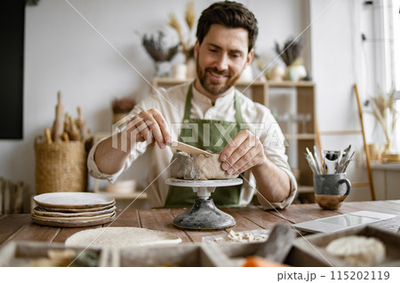 Smiling man working in a home pottery studio with laptop Smiling man working in a home pottery studio with laptop 115202119