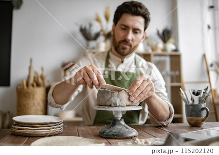 Smiling man working in a home pottery studio with laptop 115202120