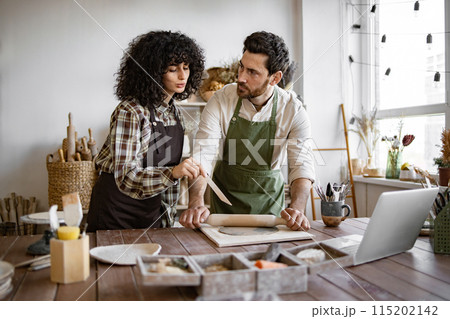 Man rolling clay while woman instructs in pottery studio Man rolling clay while woman instructs in pottery studio 115202142