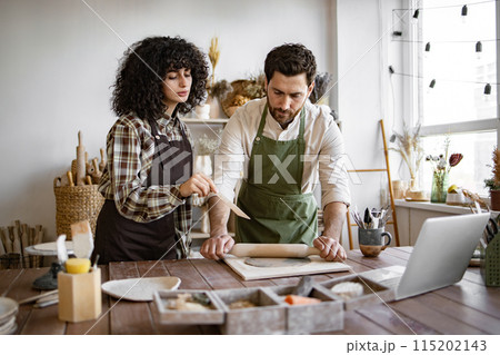 Man rolling clay while woman instructs in pottery studio 115202143