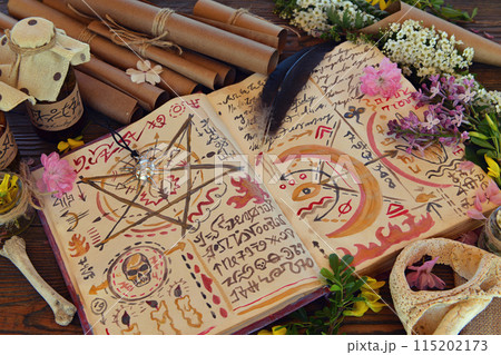 Mystic still life with magic book of spells, paper scrolls and witchy ritual objects on old table. Occult, esoteric, wicca and divination concept. No foreign language, all symbols are fictional Mystic still life with magic book of spells, paper scrolls and witchy ritual objects on old table. Occult, esoteric, wicca and divination concept. No foreign language, all symbols are fictional 115202173