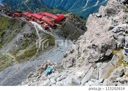槍ヶ岳の穂先の岩場を登る女性登山者と槍ヶ岳山荘 115202614