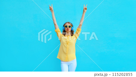 Happy modern young woman listening to music with headphones having fun on blue background Happy modern young woman listening to music with headphones having fun on blue background 115202855
