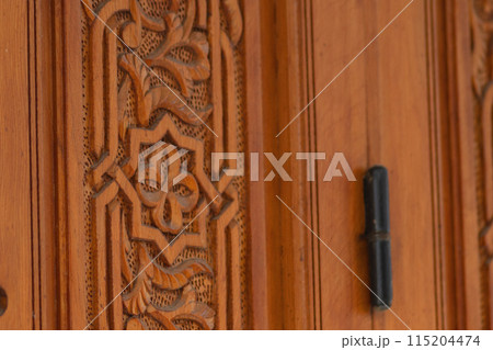 Eight-pointed star on the decoration element of a massive wooden door, hand-carved wood, as an element of traditional symbols. Eight-pointed star on the decoration element of a massive wooden door, hand-carved wood, as an element of traditional symbols. 115204474