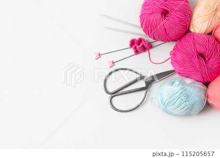 Composition of pink, blue, beige balls of knitting thread, knitting needles and scissors on gray background with place for text. Concept of home needlework, hobby for knitting warm clothes Composition of pink, blue, beige balls of knitting thread, knitting needles and scissors on gray background with place for text. Concept of home needlework, hobby for knitting warm clothes 115205657