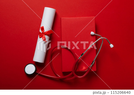 Graduate hat with diploma and stethoscope, on red background. Graduate hat with diploma and stethoscope, on red background. 115206640