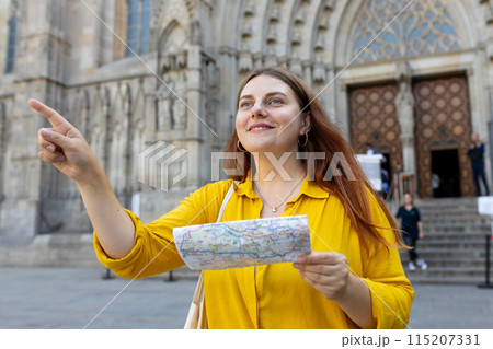 Young woman tourist with paper map standing in front of the famous saint Eulalia church in Barcelona. Concept of travel, tourism and vacation in city. Cathedral of Barcelona 115207331