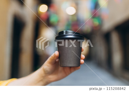 Woman gives paper black coffee cup or tea on urban background. Take away or delivery concept. Copy space. Place for your text on mug, mockup. Woman gives paper black coffee cup or tea on urban background. Take away or delivery concept. Copy space. Place for your text on mug, mockup. 115208842