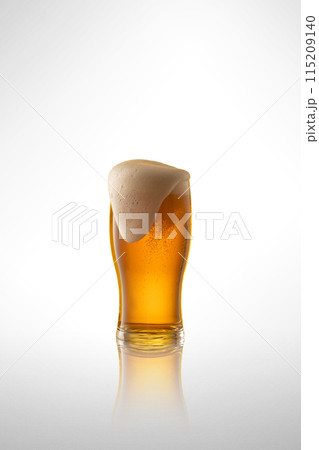 Tall glass filled with amber colored lager beer, topped with creamy white head against white studio background. Tall glass filled with amber colored lager beer, topped with creamy white head against white studio background. 115209140