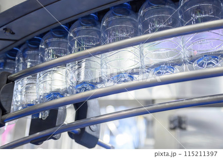 The empty drinking water bottles hanging on the conveyor belt for filling process. The empty drinking water bottles hanging on the conveyor belt for filling process. 115211397