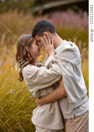 Happy couple on autumn walk outdoors. Two lovers in autumn park. Love and tender touch. Gentle hugs. Young man and woman in classic autumn colors outfit on a romantic date in a cozy park. Young girl 115211681