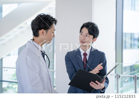 病院で笑顔で会話する男性医師と医薬情報担当者MR 115212833