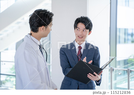 病院で笑顔で会話する男性医師と医薬情報担当者MR 115212836