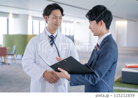 病院で笑顔で会話する男性医師と医薬情報担当者MR 115212839