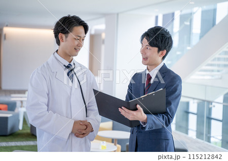 病院で笑顔で会話する男性医師と医薬情報担当者MR 115212842