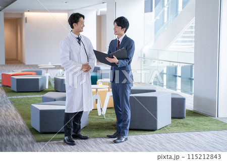 病院で笑顔で会話する男性医師と医薬情報担当者MR 115212843