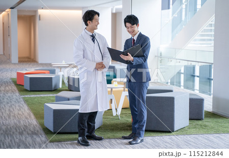 病院で笑顔で会話する男性医師と医薬情報担当者MR 115212844