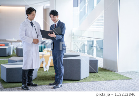 病院で笑顔で会話する男性医師と医薬情報担当者MR 115212846