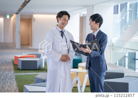 病院で笑顔で会話する男性医師と医薬情報担当者MR 115212857