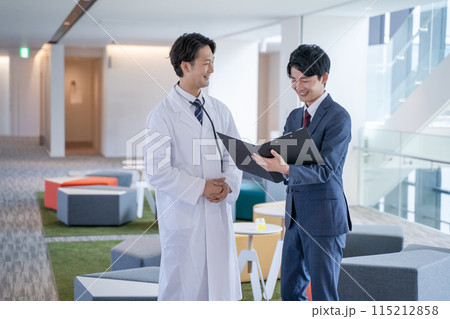 病院で笑顔で会話する男性医師と医薬情報担当者MR 115212858