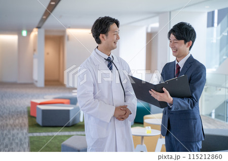 病院で笑顔で会話する男性医師と医薬情報担当者MR 115212860