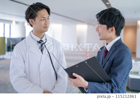 病院で笑顔で会話する男性医師と医薬情報担当者MR 115212861