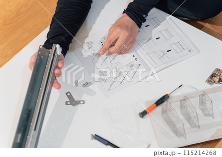 Hands of a woman assembling a metal piece of furniture following instructions 115214268
