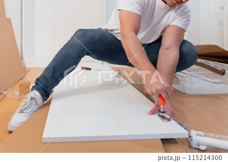 Professional carpenter assembling furniture on parquet floor of a new apartment Professional carpenter assembling furniture on parquet floor of a new apartment 115214300
