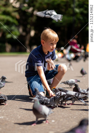 Cute little boy feeding pigeons in the city park. Selective focus. 115214962