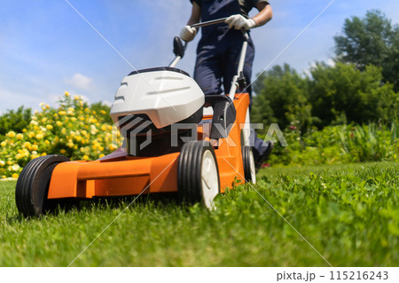 A professional gardener with a lawnmower cares for the grass in the backyard. A professional gardener with a lawnmower cares for the grass in the backyard. 115216243