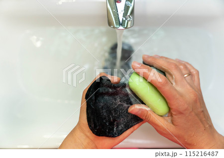 A person hand washing black socks in a bathroom sink with soap 115216487