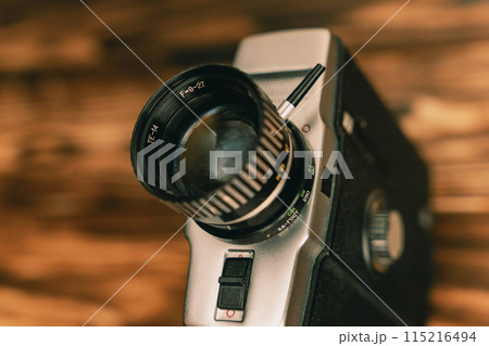 Close-up of a vintage film camera lens on a wooden background, 8mm Close-up of a vintage film camera lens on a wooden background, 8mm 115216494