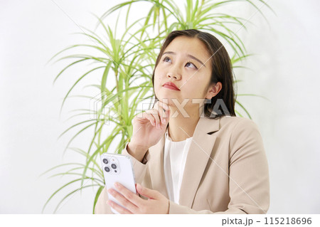 オフィスで考えながらスマホを使う若いビジネスウーマン 115218696