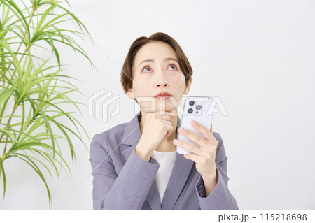 オフィスで考えながらスマホを使うビジネスウーマン オフィスで考えながらスマホを使うビジネスウーマン 115218698
