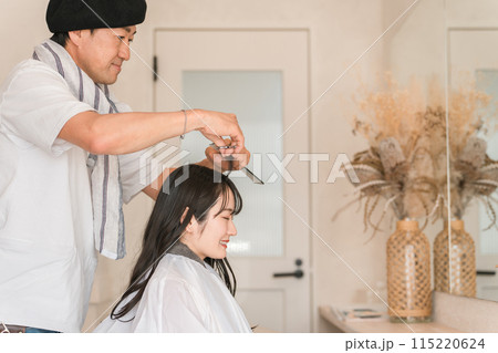 美容室・美容院・ヘアサロンでヘアカットしてもらう若い女性客と男性美容師・スタイリスト 115220624