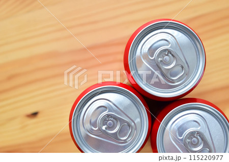 three aluminium red cans of soft drink put on brown wooden table three aluminium red cans of soft drink put on brown wooden table 115220977