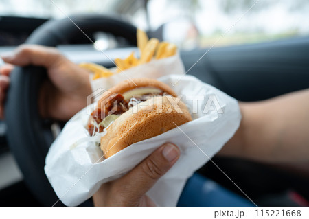 Asian lady holding hamburger to eat in car, dangerous and risk an accident. Asian lady holding hamburger to eat in car, dangerous and risk an accident. 115221668